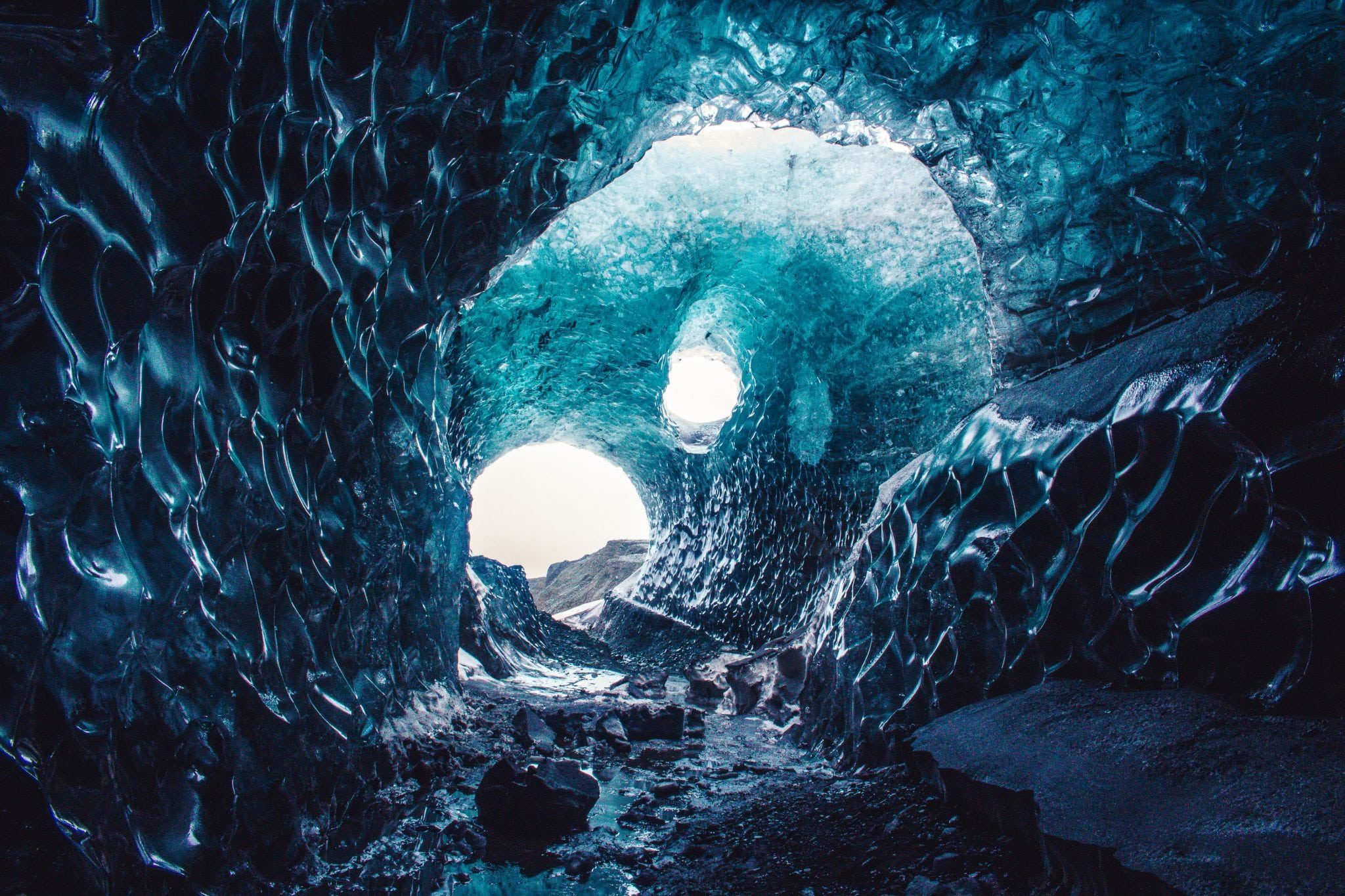 Ice cave interior with dramatic blue ice formations and tunnel leading to light